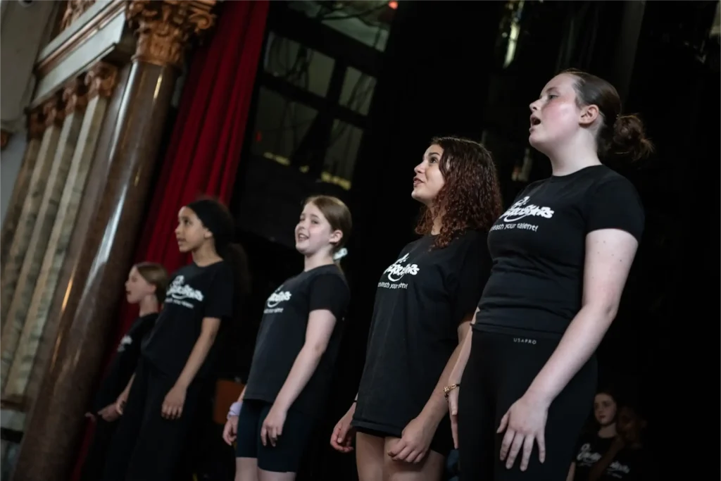 Senior students from Cherry Stars Stage and Screen School singing on stage in branded black t-shirts during performance at Stanley Arts.