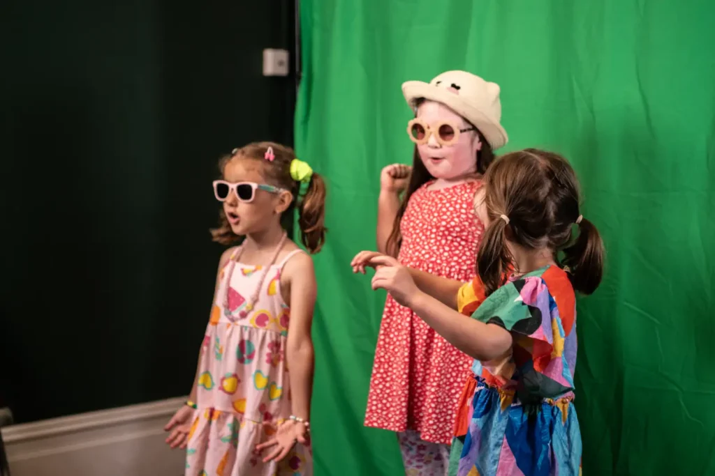 Children in costume performing in front of a green screen during a drama class workshop